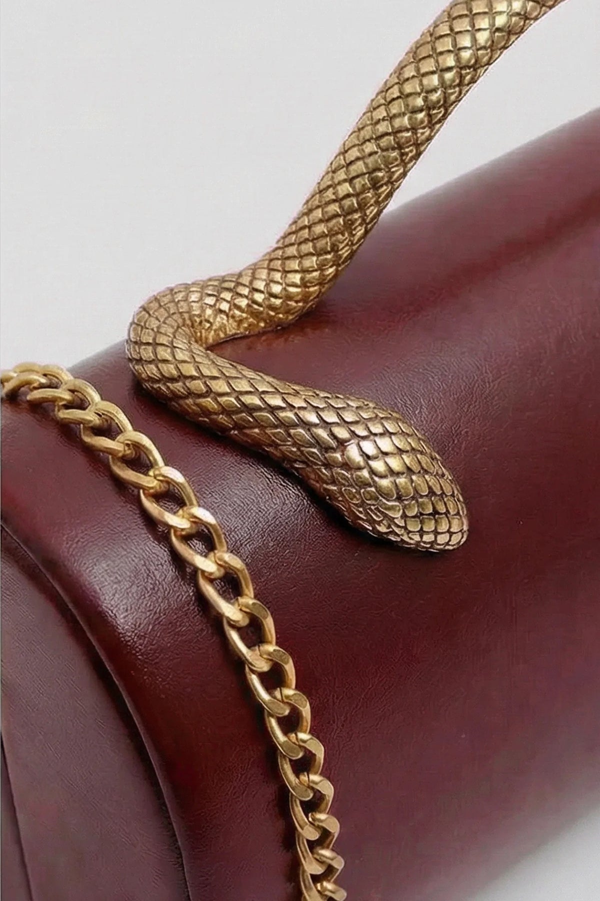 BOLSO DE MANO ESTRUCTURADO CON ASA DE SERPIENTE Y CADENA DORADA - GRANATE